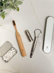 Tongue scraper beside a metal travel case open for cleaning and storage