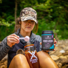 Wilderness Athlete Hydrate & Recover grape powder being dispensed for post-workout hydration.