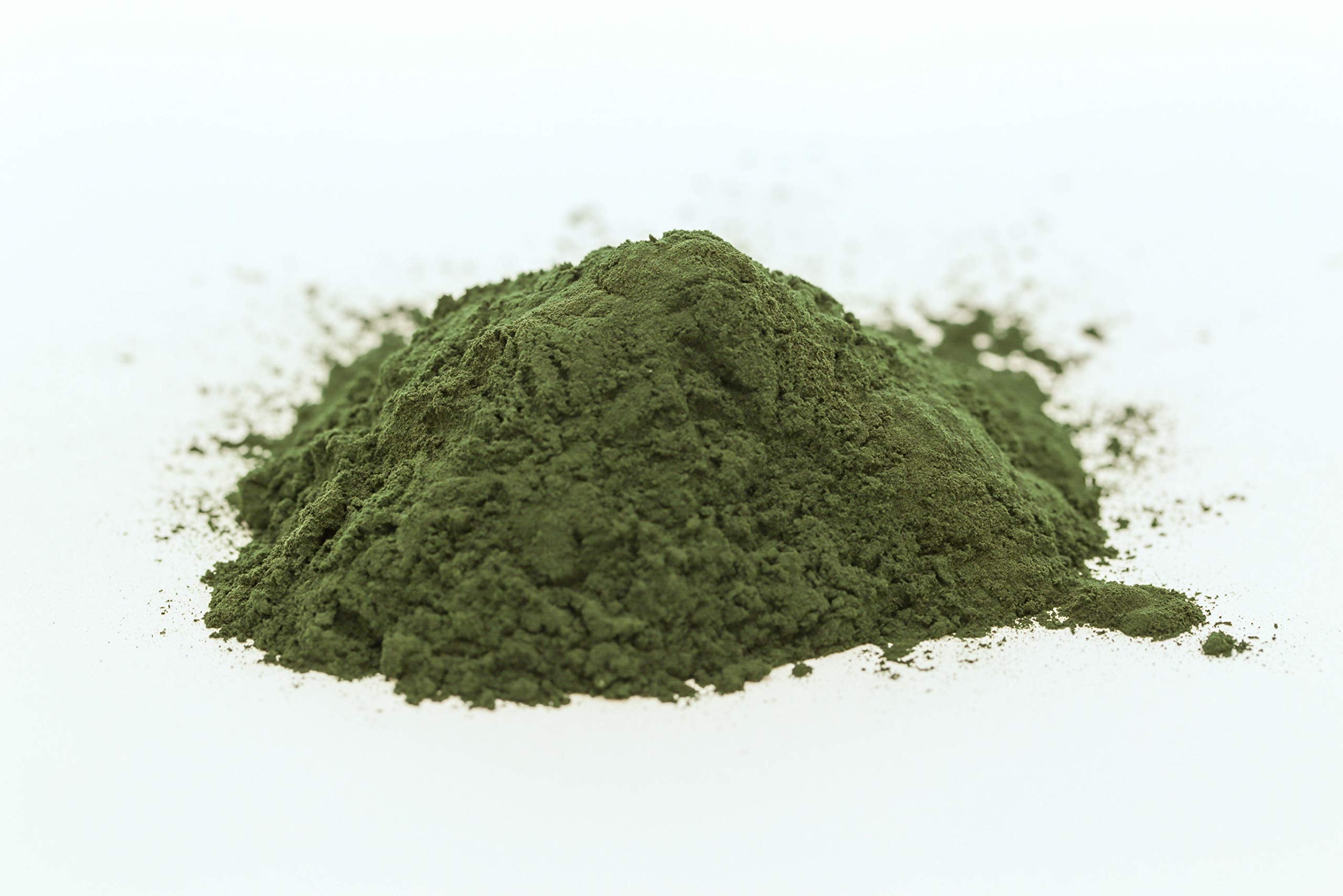 Spoon with spirulina powder next to a glass illustrating usage