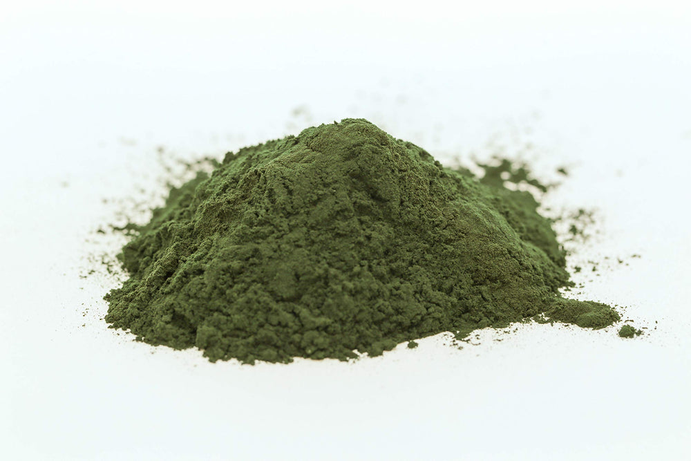 Spoon with spirulina powder next to a glass illustrating usage